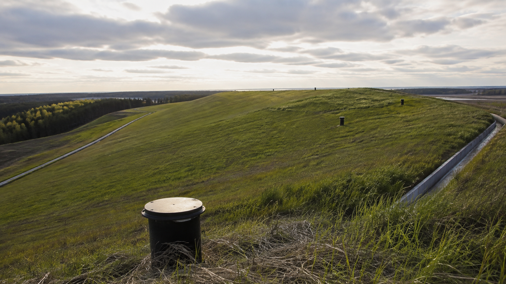 Collina di discarica esaurita con copertura finale rinverdita, canaline di drenaggio delle acque meteoriche e teste di pozzo di captazione del biogas
